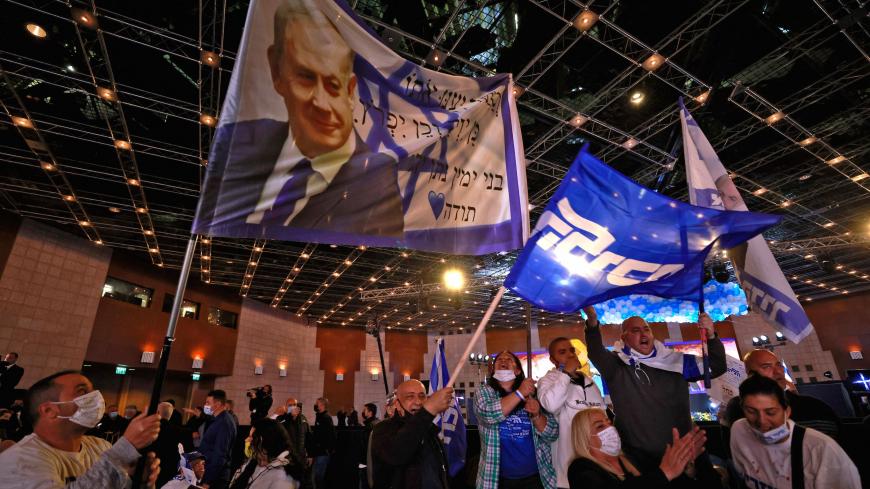 Likud party supporters wave flags bearing the party's leader, Prime Minister Benjamin Netanyahu, as they react at their party campaign headquarters in Jerusalem on March 23, 2021