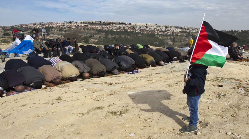 A young boy holds a flag as people pray during a protest of Palestinian activists over confiscated lands by the Israeli army in Beit Iksa, West Bank, Jan. 25, 2013.