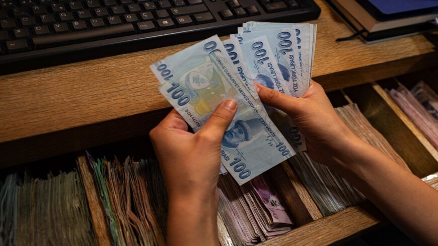 A currency exchange office worker counts Turkish Lira banknotes in front of the electronic panel displaying currency exchange rates at an exchange office in Istanbul, on August 6, 2020.