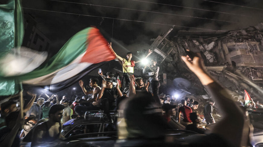 People wave the Palestinian flag as they celebrate in front of a destroyed building in Gaza City early on May 21, 2021, following a cease-fire brokered by Egypt between Israel and the ruling Islamist movement Hamas in the Gaza Strip.