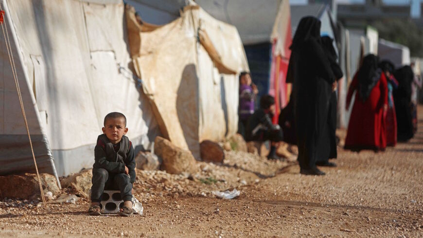 A child sits near displaced Syrians lining up to collect plates of food prepared by a local charity for the Ramadan fast-breaking meal at a camp for people displaced by conflict in the town of Sarmada in Syria's northwestern Idlib province on April 13, 2021. 