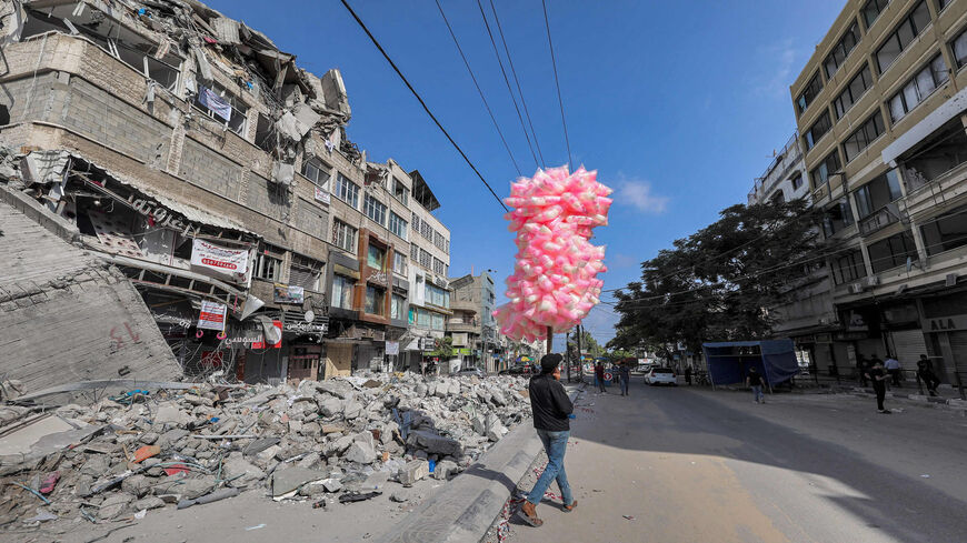 A Palestinian pedlar walks with bags of cotton candy past the rubble of a building destroyed during the May 2021 conflict between Hamas and Israel in al-Rimal neighborhood, Gaza City, Gaza Strip, June 10, 2021.