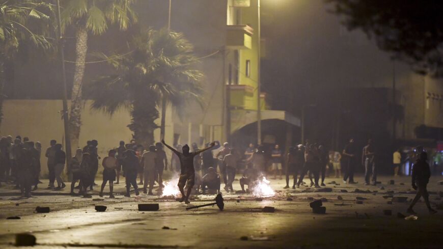 Protesters blocking a street gesture as Tunisian security forces fire tear gas in the Sidi Hassine suburb on the northwestern outskirts of Tunis on June 12, 2021, amid outrage against policing practices following the death of a youth.