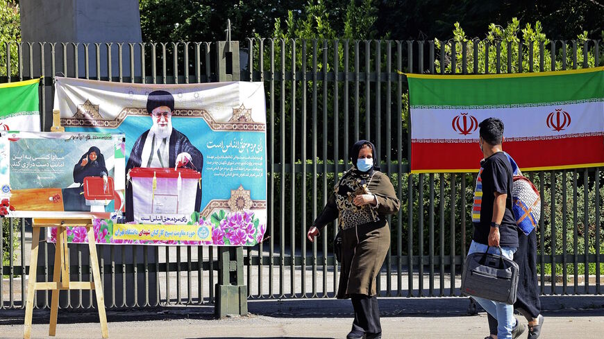 Iranians walk past banners encouraging people to vote hung on a fence at Tehran university in the eponymous capital, on June 14, 2021, ahead of the June 18 presidential elections. 