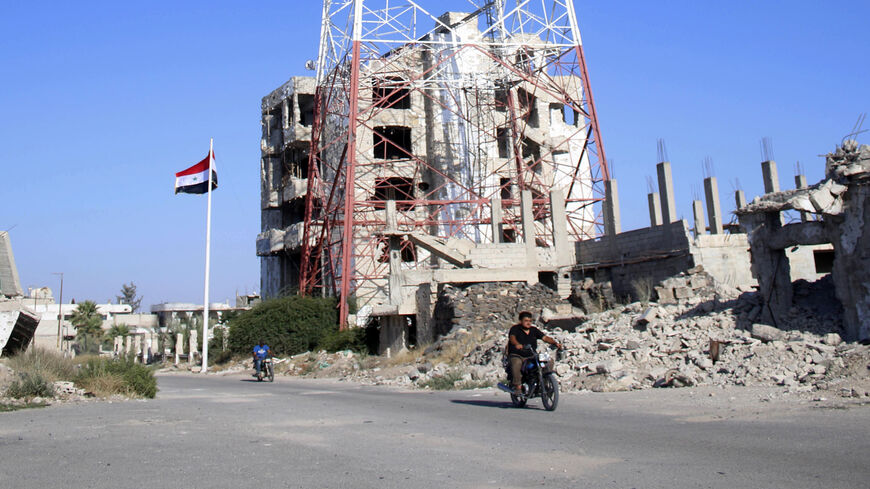 A man rides a scooter in front of the Syrian national flag, raised in a street in Daraa-al-Balad, an opposition-held part of the southern city of Daraa, Syria, July 12, 2018.