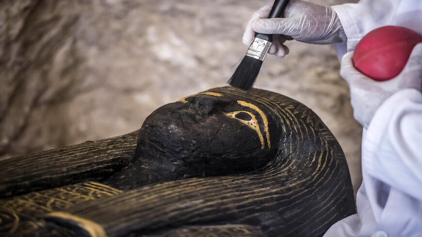 An Egyptian archaeologist brushes the top of a carved black wooden sarcophagus inlaid with gilded sheets, dating to Egypt's Late Period (7th-4th century BC), on the west bank of the Nile north of the southern city of Luxor, Egypt, Nov. 24, 2018.