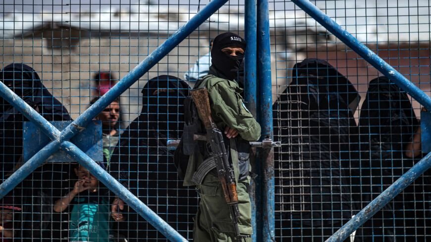 A fighter from the Syrian Democratic Forces (SDF) guards a gate as Syrian women wait inside the Kurdish-run al-Hol camp.