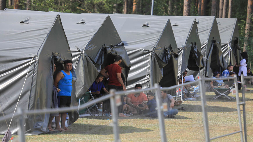 Migrants are seen through a fence as they stand and sit by tents in a camp near the border town of Kapciamiestis, Lithuania, July 18, 2021.