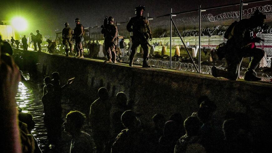 British and Canadian soldiers stand guard near a canal in the late hours of Aug. 22, 2021, as Afghans wait outside the foreign military-controlled part of the airport in Kabul