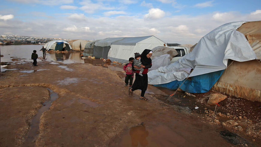 A Syrian woman walks by tents at a camp for the internally displaced, near the town of Kafr Lusin, Idlib province, Syria, Jan. 19, 2021.