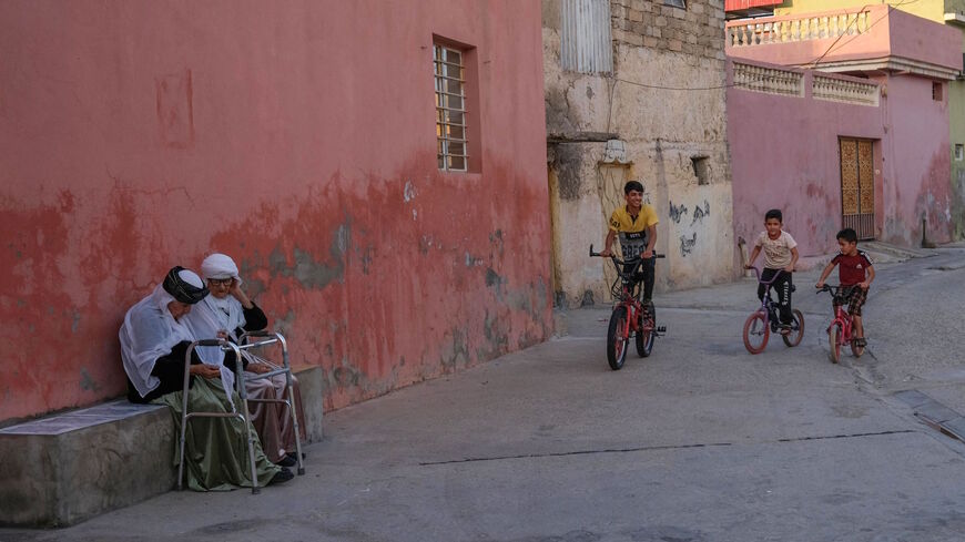 Iraqi Yazidi children ride bicycles as elderly women sit on a ramp in the town of Sheikhan, some 50km northeast of Mosul, on July 15, 2021.
