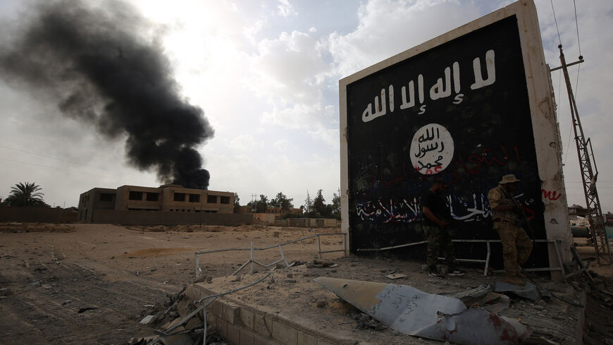 Iraqi fighters of the Hashed al-Shaabi (Popular Mobilisation units) stand next to a wall bearing the Islamic State (IS) group flag as they enter the city of al-Qaim, in Iraq's western Anbar province near the Syrian border as they fight against remnant pockets of Islamic State group jihadists on Nov. 3, 2017. 