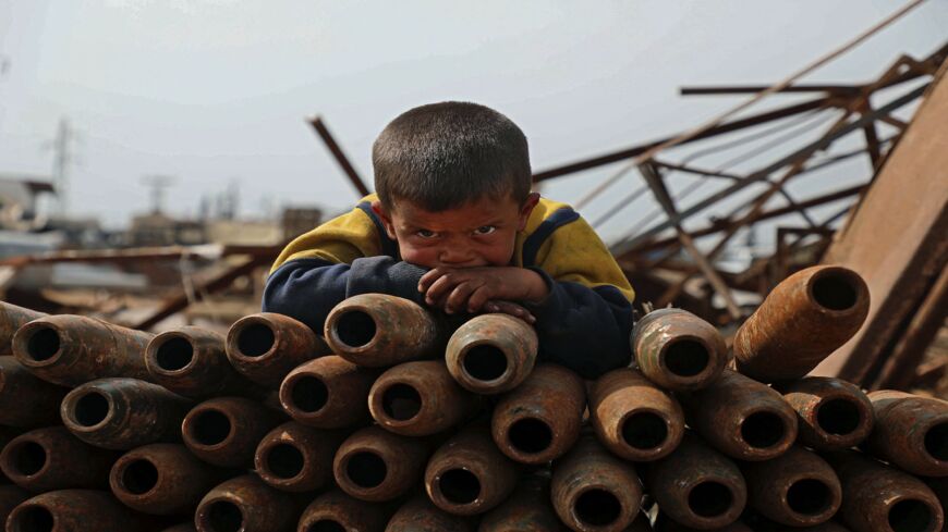 A Syrian child poses atop a stack of neutralized shells at a metal scrapyard on the outskirts of Maaret Misrin town in the northwestern Idlib province, on March 10, 2021.