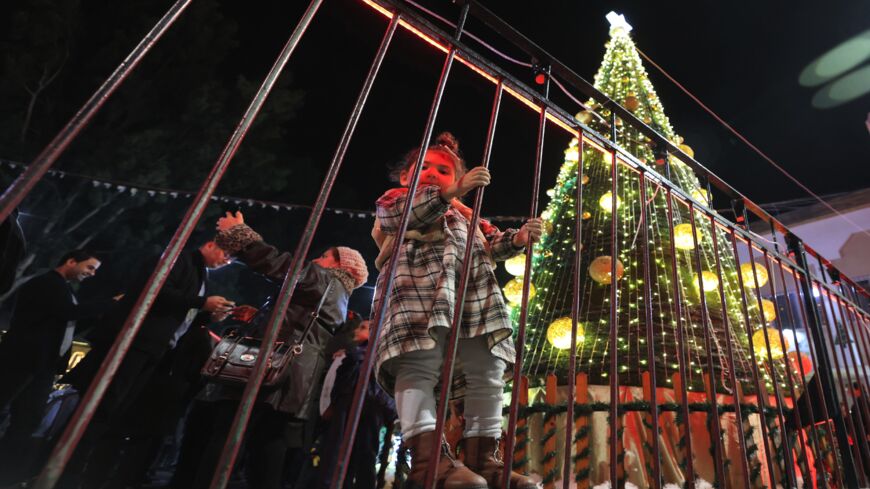 A girl holds on to a fence as she stands near the lit-up Christmas tree in the courtyard of the YMCA Gaza in Gaza City on Dec. 10, 2021.