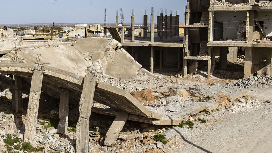 People sit on the ground by a destroyed building in the Kurdish town of Kobani, in the north of Aleppo governorate, Syria, Feb. 25, 2021.