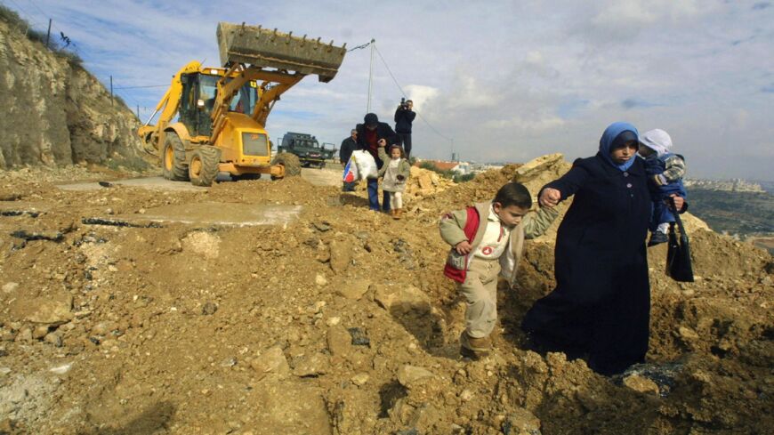 Palestinians walk along a demolished road leading to the Palestinian village of al-Walaja south of Jerusalem, Jan. 11, 2004.