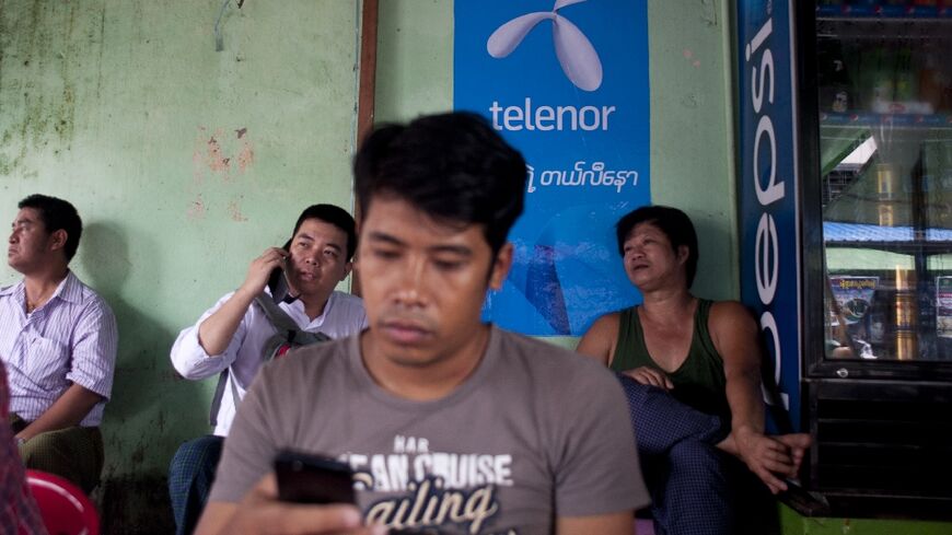 A man uses a phone in front of a Telenor advertising board in Yangon