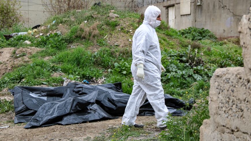 A worker walks past the covered remains of bodies unearthed from a mass grave in the northern Iraqi city of Mosul