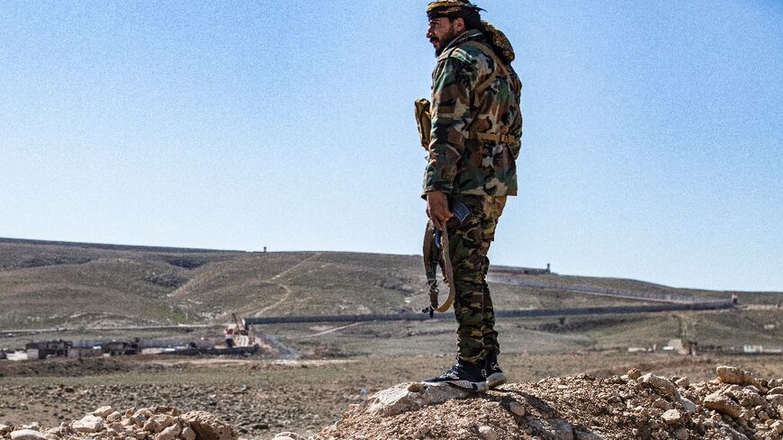 A member of the border guard force loyal to the Syrian Democratic Forces (SDF) looks on near Syria's town of al-Hol at ongoing construction of a concrete border fence being erected on the Iraqi side