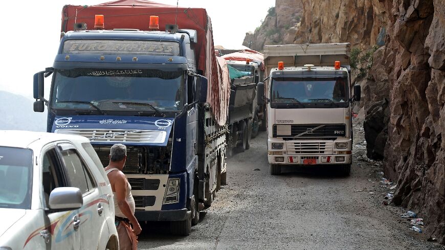 Trucks travel along a heavily damaged road, the only route between Yemen's cities of Taez and Aden