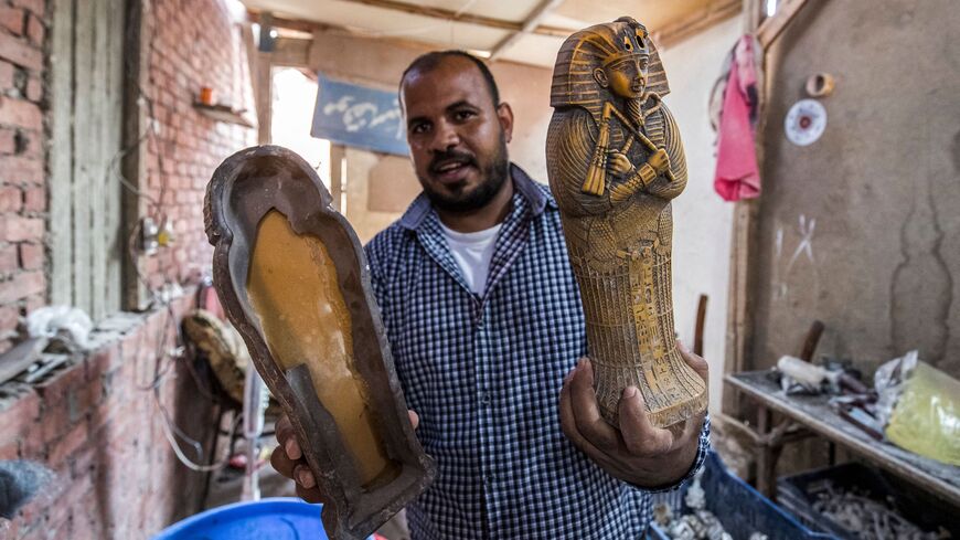 Eid Yosri, an artifact replica craftsman, poses for a photo with a mini sarcophagus of his own creation.