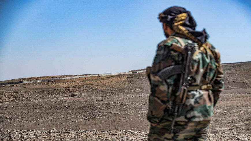 A member of the border guard force loyal to the Syrian Democratic Forces looks from a position in the countryside near the town of al-Hol at construction work on a concrete border fence erected on the Iraqi side, Hasakah province, Syria, March 29, 2022.