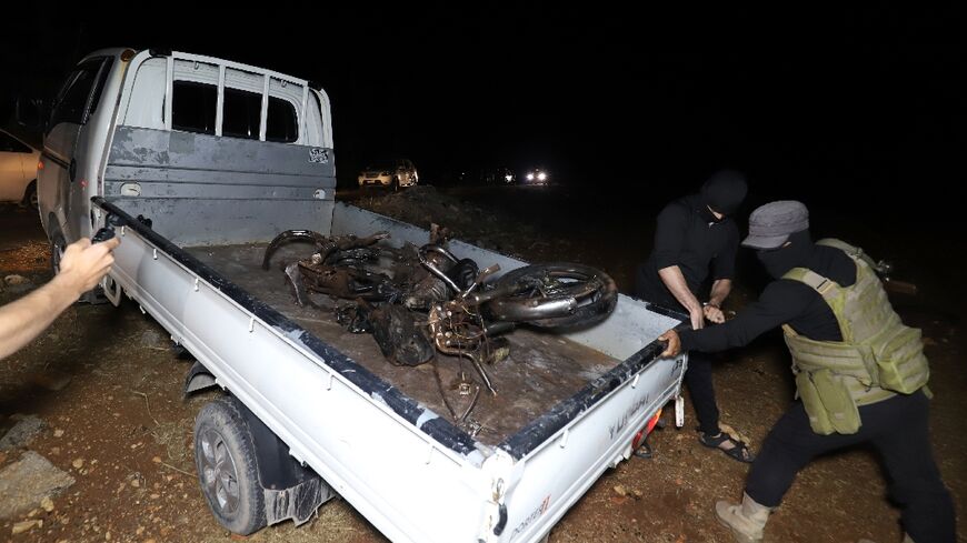 Fighters of jihadist group Hayat Tahrir al-Sham, which dominates northwestern Syria, carry away a mangled motorcyle after a US drone strike targeting a leader of a rival, Al-Qaeda-linked faction, Hurras al-Deen