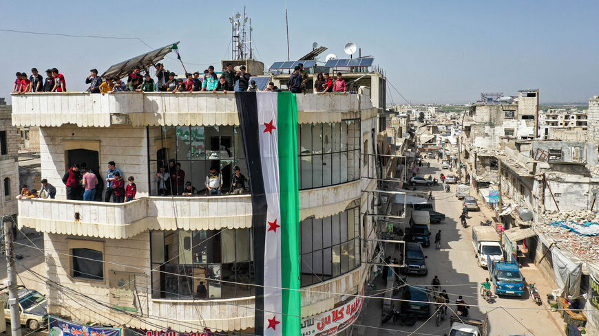 An aerial view of protesters raising a giant flag of the Syrian rebels atop a building during a demonstration against Russia's invasion of Ukraine, Binnish, Idlib province, Syria, April 1, 2022.