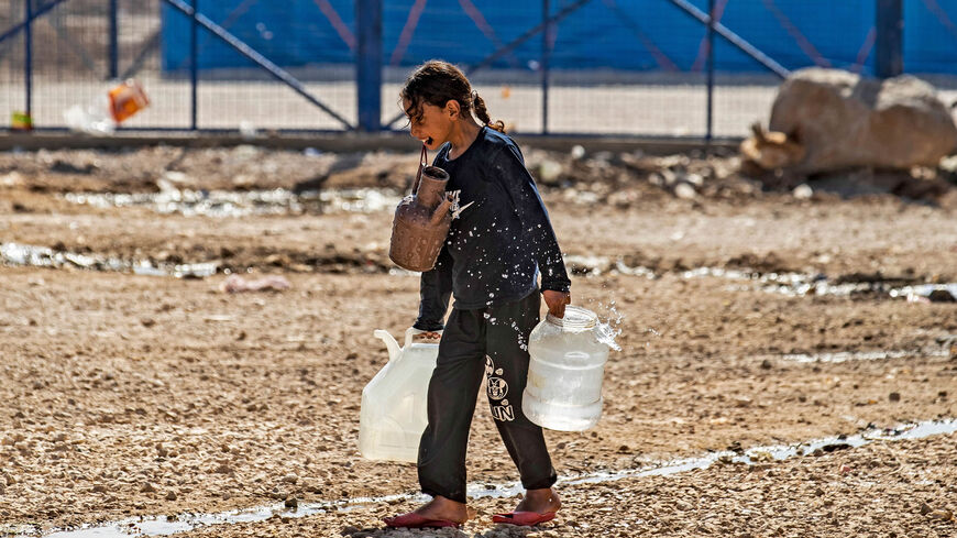 A girl walks while holding water containers in her hands and mouth at the Washukanni camp for the internally displaced near the town of Tuwaynah, near the city of Hasakah, Syria, Oct. 8, 2020.