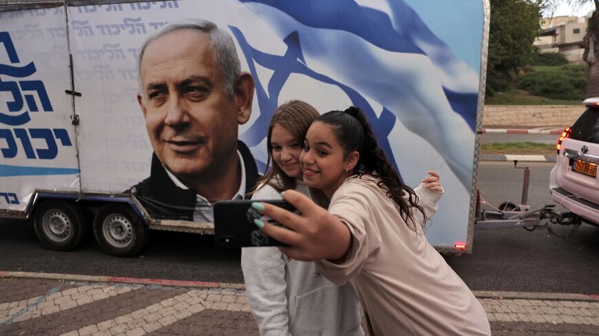 Two girls pose for a selfie photo before a vehicle showing Israel's former prime minister Benjamin Netanyahu, ahead of November 1 general elections