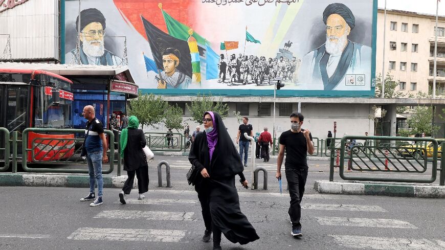 Iranians pass a billboard showing Iran's supreme leader Ayatollah Ali Khamenei and Ayatollah Ruhollah Khomeini (R) in Tehran, before the anti-regime protest movement began in September 2022