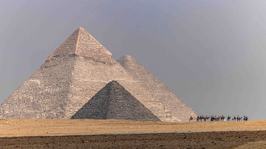 Tourists ride camels at the Giza pyramids necropolis with (foreground to background) the Pyramid of Menkaure (Menkheres), Pyramid of Khafre (Chephren) and Great Pyramid of Khufu (Cheops), Giza, Egypt, Oct. 27, 2022.