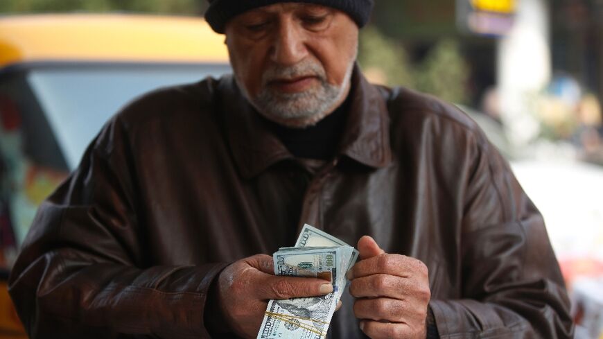 A man counts US dollar banknotes in a Baghdad market on December 27, 2022 as the value of Iraqi dinar against US dollar drops further.