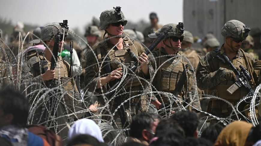 US soldiers stand guard behind barbed wire as Afghans sit on a roadside near the military part of the airport in Kabul on August 20, 2021, hoping to flee from the country after the Taliban's military takeover of Afghanistan