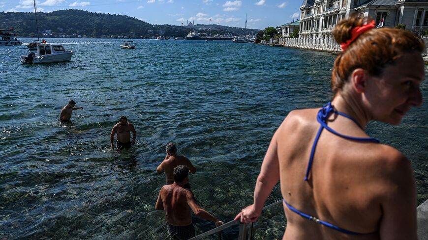 wimmers enter the water in the Bosphorus strait in Istanbul's Bebek district on July 29, 2022. - Istanbul, a historic megalopolis of 16 million people resting between two continents and two sea, does not bring to mind immediate images of a beach resort. But just like the locals of New York, Beirut and a handful of other global cities, Istanbulites can swim all summer long and return home on the metro with salt layering their skin, sand trapped under their sandals. (Photo by Ozan KOSE / AFP) (Photo by OZAN K