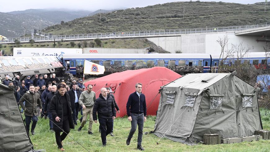 Greek Prime Minister Kyriakos Mitsotakis (R) visits the area of a crushed wagon.