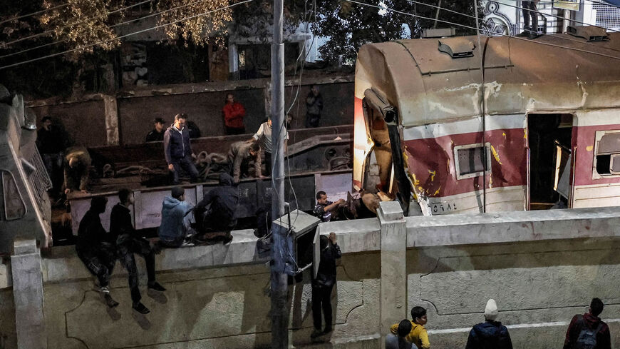 People gather by a wall fencing the railway track as a crane is deployed to lift a derailed train at the scene of a railroad accident, Qalyub, Qalyub province, Egypt, March 7, 2023.