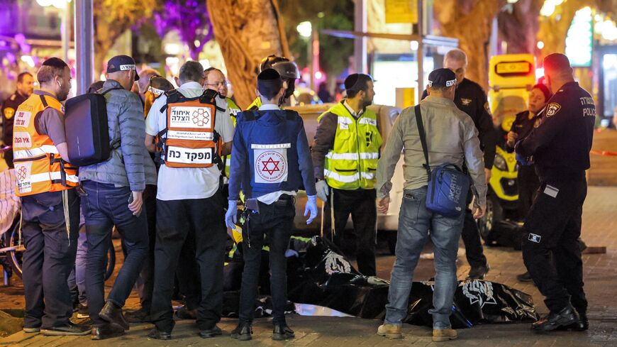 Israeli police and paramedics stand before a dead body in a bag at the scene of a shooting attack.