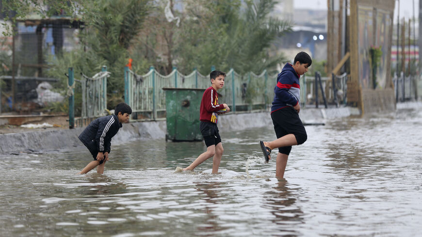 Iraqi children cross a flooded street in the Iraqi capital Baghdad after heavy rains, on Dec. 24, 2022.