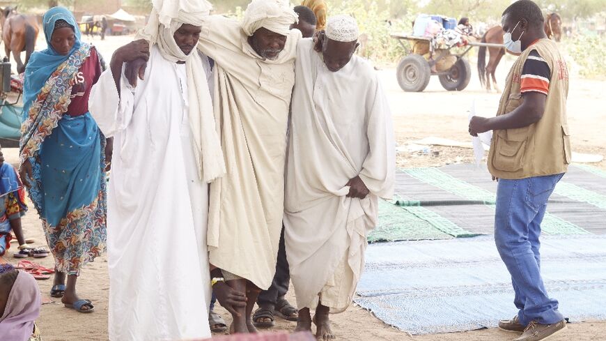 Two men assist an elderly Sudanese refugee who crossed into Chad to flee fighting in the Darfur region of Sudan