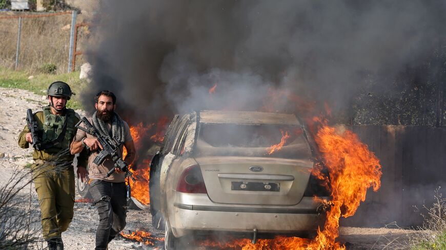 TOPSHOT - A member of Israeli security forces and one from settlement security walk past a burning car reportedly set on fire by settlers from the nearby Bracha settlement, in the Palestinian Burin village in the occupied West Bank on February 25, 2023. (Photo by jaafar ashtiyeh / AFP) (Photo by JAAFAR ASHTIYEH/AFP via Getty Images)