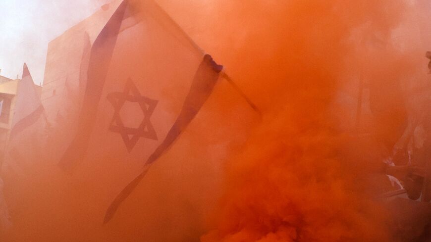 An Israeli flag flown by a demonstrator is surrounded by smoke from flares during a protest against the Israeli government's judicial overhaul bill