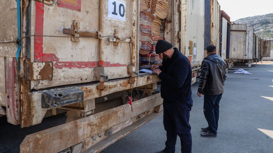 A clerk inspects the cargo of a truck among a convoy carrying tent and shelter kits.