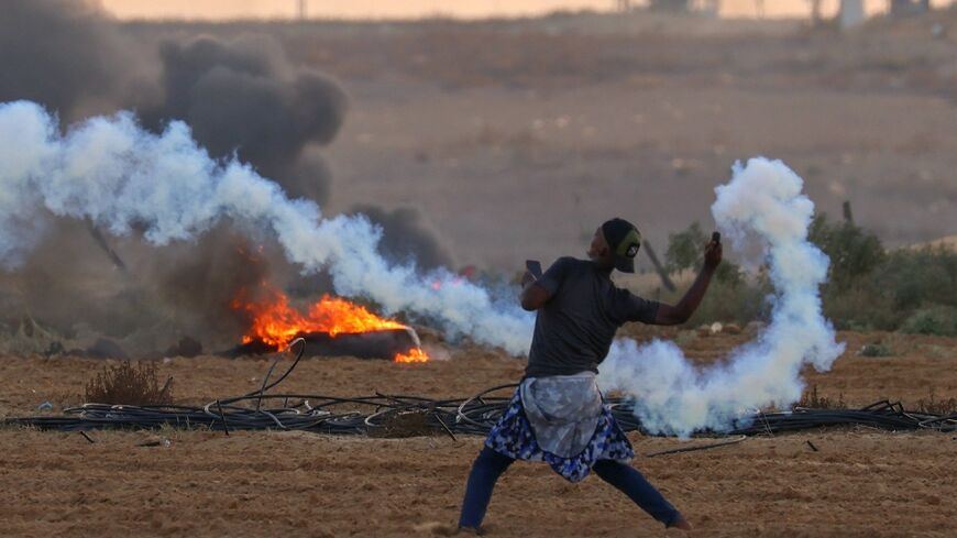 A Palestinian demonstrator throws back a tear gas canister fired by Israeli troops during clashes along the Gaza border