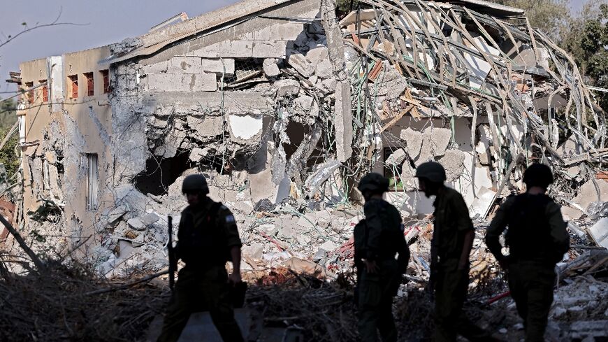 Israeli soldiers walk past a destroyed house in kibbutz Beeri 