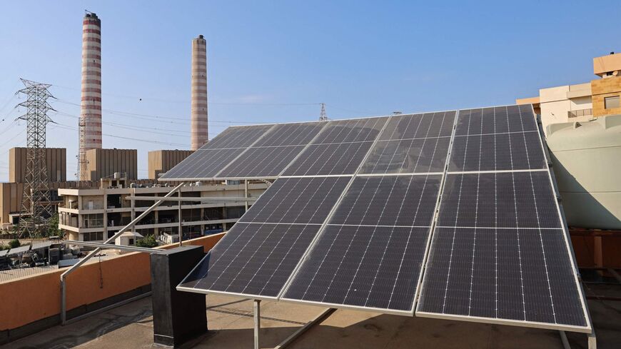 Solar panels are installed on a rooftop near the red-and-white chimneys of a power plant in the industrial district of Zouk Mikael, where residents believe they are more likely to develop cancer than elsewhere in the country because of air pollution, north of Lebanon's capital Beirut on October 10, 2022. - A Greenpeace study found that the surrounding Jounieh area ranked fifth in the Arab world and 23rd globally for cities most contaminated by nitrogen dioxide, a dangerous pollutant released when fuel is bu