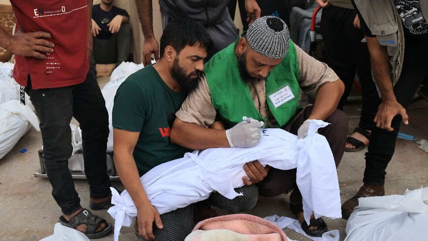 A man writes the name on the shroud of a child killed in an Israeli strike on Deir Balah in central Gaza