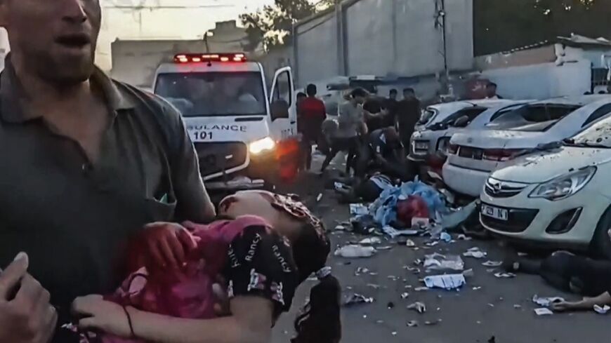 In this image grab taken from an AFPTV video footage shows a man carrying an injured girl near an ambulance damaged in a reported Israeli strike in front of Al-Shifa hospital in Gaza City on November 3, 2023