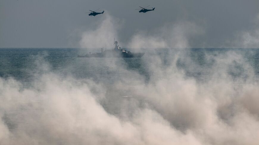 Russian army Mi-24 helicopters fly above a warship at the Turali range on the Caspian Sea coast in the Republic of Dagestan in Southern Russia on September 23, 2020 during the "Caucasus-2020" military drills gathering China, Iran, Pakistan and Myanmar troops, along with ex-Soviet Armenia, Azerbaijan and Belarus. - Up to 250 tanks and around 450 infantry combat vehicles and armoured personnel carriers will take part in the September 21 to 26 land and naval exercises that will involve 80,000 people including