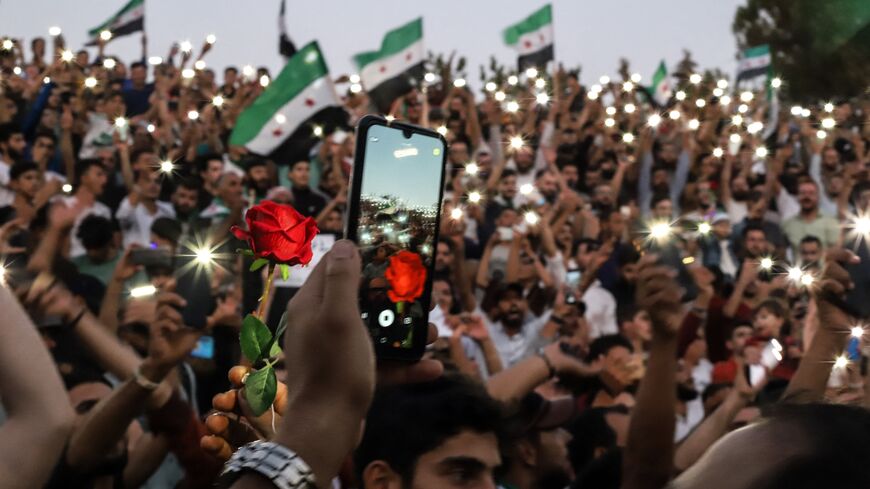 A man snaps a picture of a red rose raised by a protestor, during a demonstration in Syria's rebel-held northwestern city of Idlib on Aug. 25, 2023.